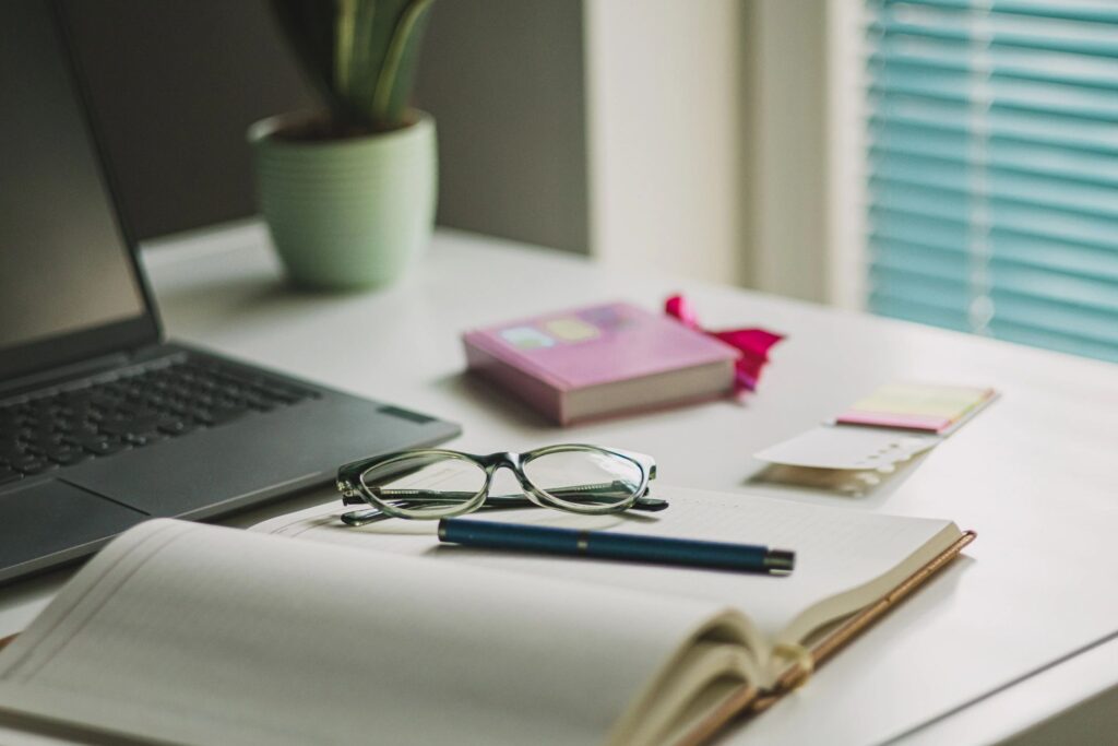 Women's office desk table. Laptop computer, cup of coffee, reading glasses and office supplies.